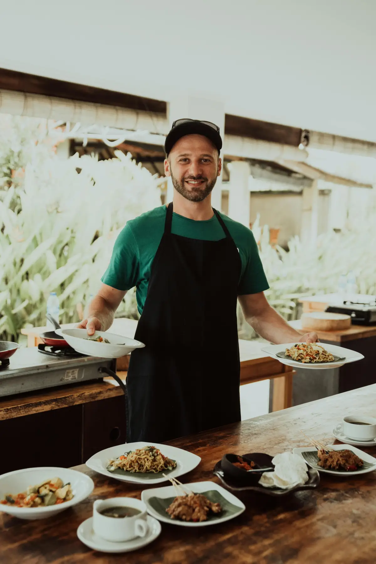 A chef in a kitchen with plates of fresh food on a wooden counter
