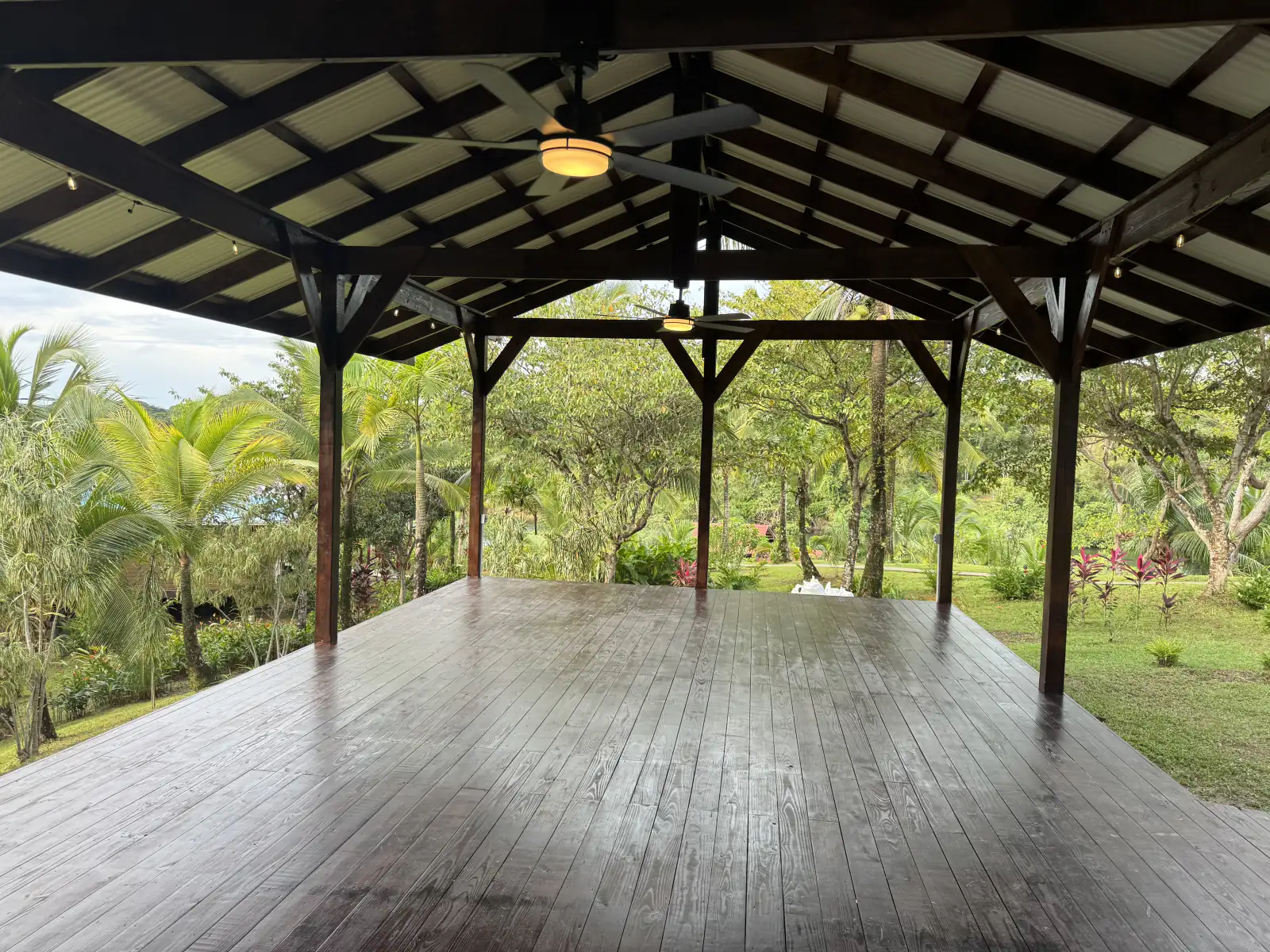 The island pavilion empty and open on three sides, a broad wood deck under a high roof, jungle all around