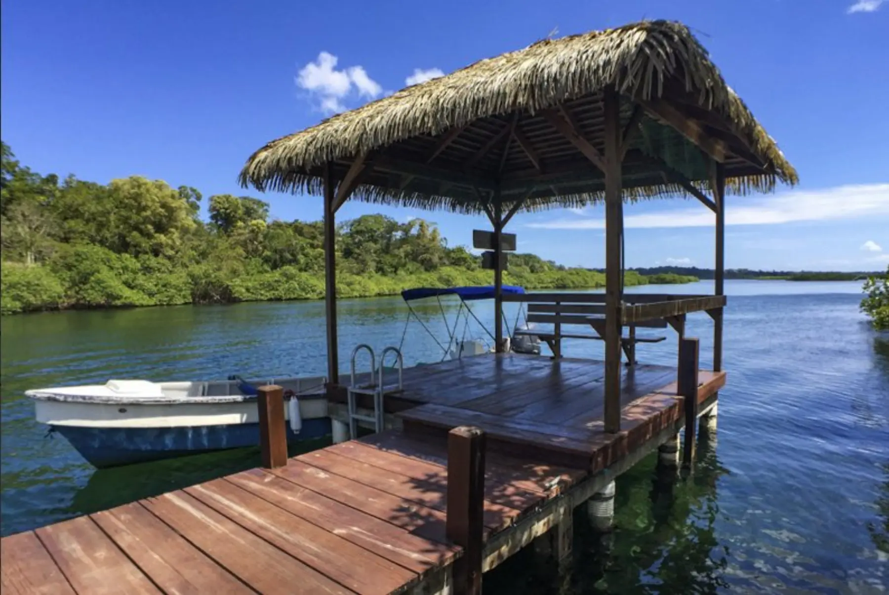 A wooden dock with a thatched-roof boat house and the water beyond